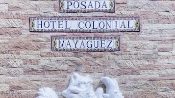 Eine Steinsäule mit dekorativer Reliefskulptur und einem Schild für 'Posada Hotel Colonial Mayaguez'.