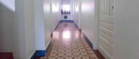A long, narrow hallway with patterned floor tiles, white walls, and a ceiling light.