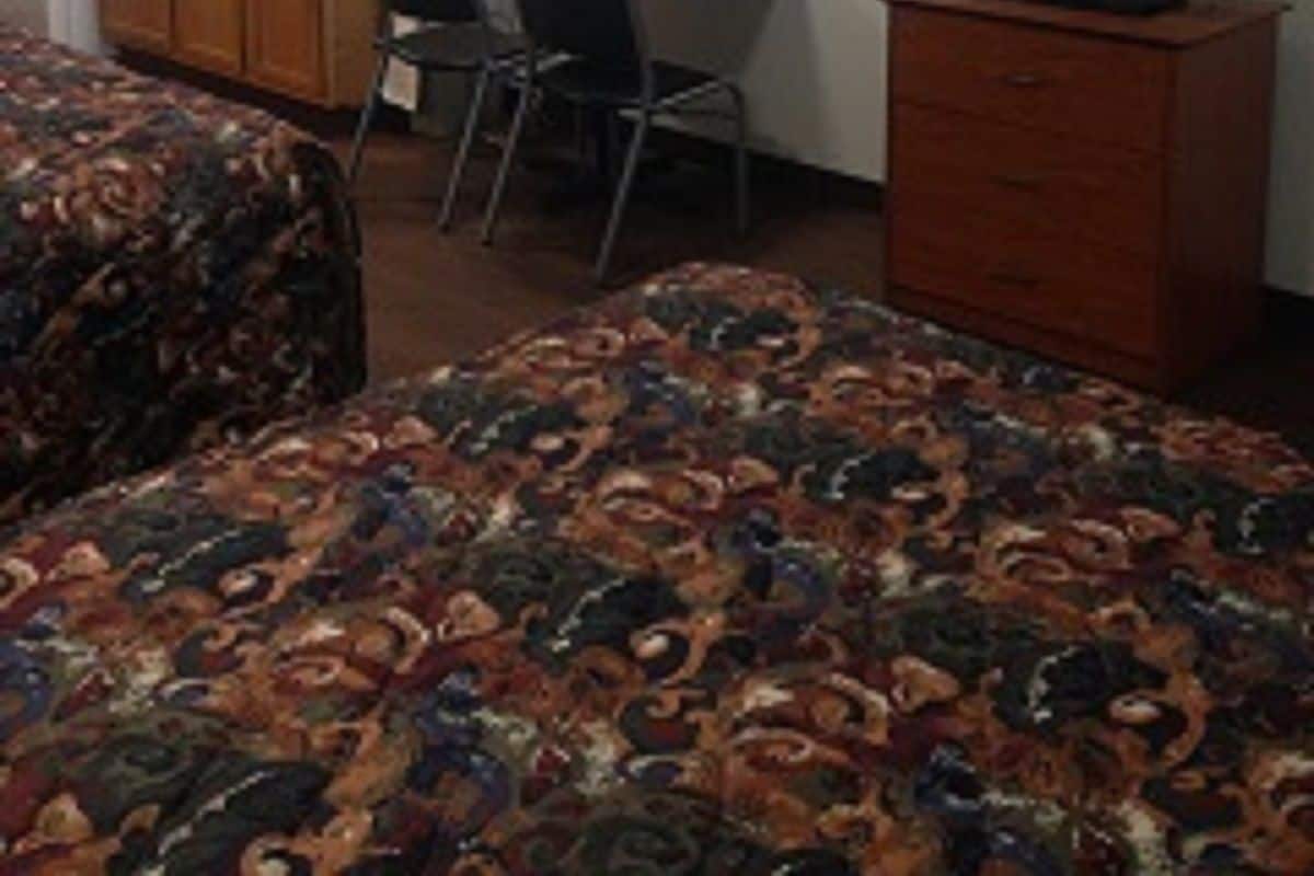 A small hotel room with a bed, a desk, a chair, a television, and a kitchenette.