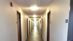 A long, narrow hotel corridor with doors on both sides, a wooden floor, and a ceiling light. - Inland Suites Lamar Street (Memphis)