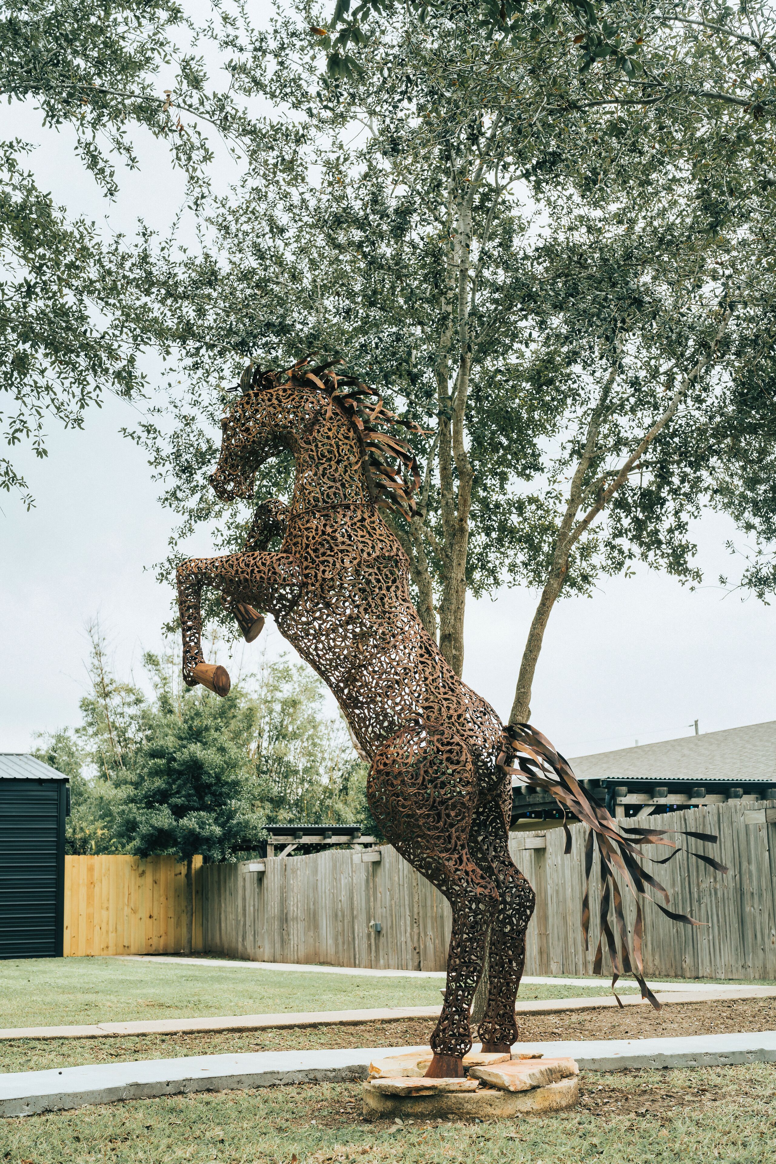 Une sculpture équestre en métal, placée dans un jardin.