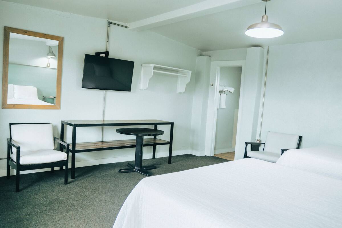Ein Hotelzimmer mit Bett, Schreibtisch, Stuhl, Fernseher und Spiegel.