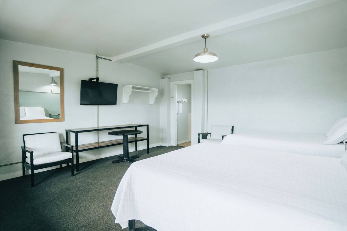 Ein Hotelzimmer mit einem großen Bett, einem Schreibtisch mit Stuhl, einem Fernseher und einem Spiegel.