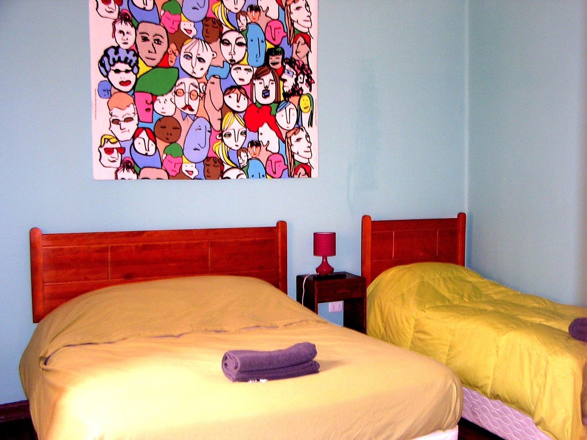Una habitación con dos camas, un cuadro de personajes de dibujos animados y una mesita de noche con lámpara.