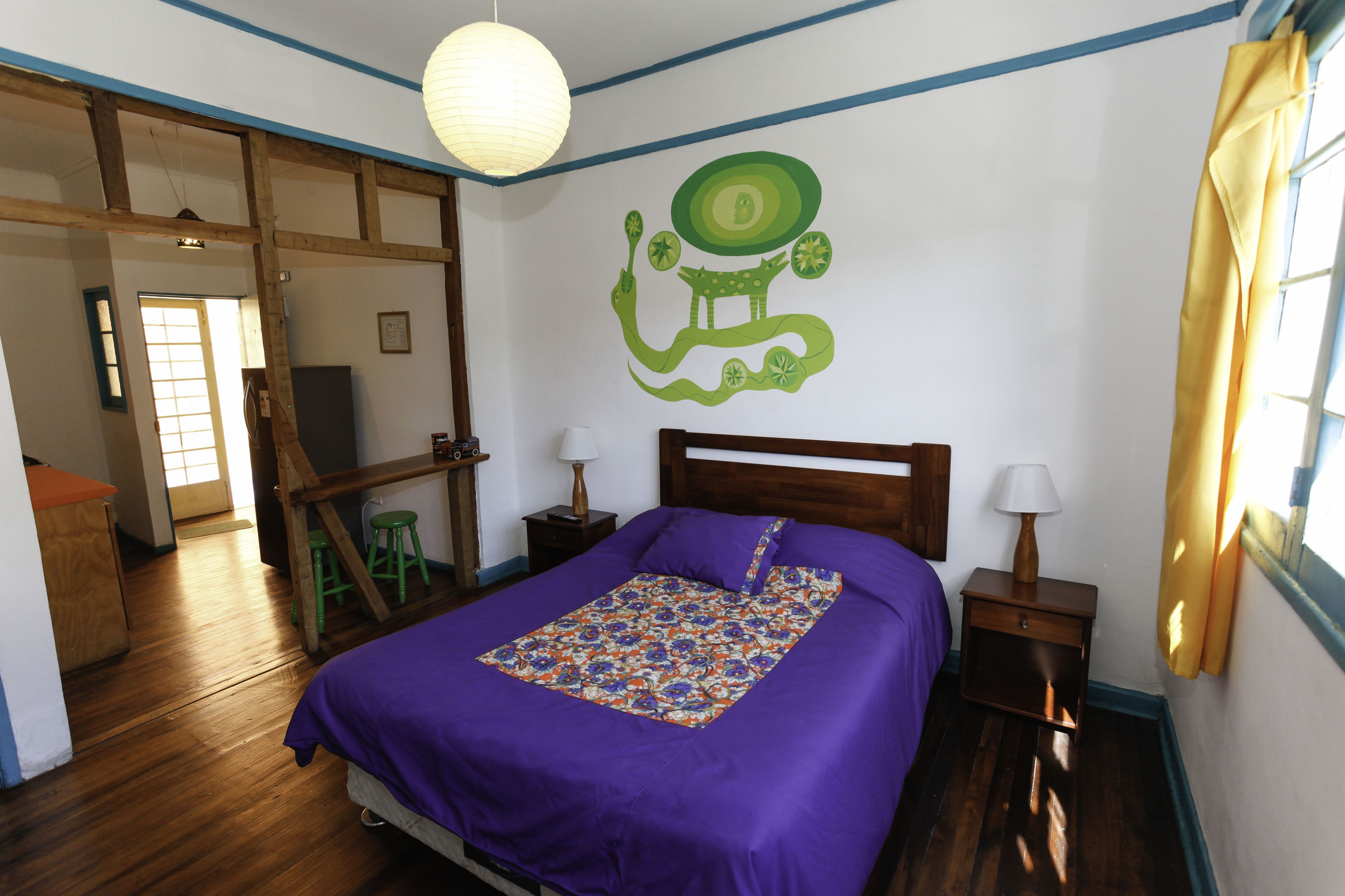 A bedroom with a bed, a nightstand, a lamp, a wall decoration, and a window with curtains.