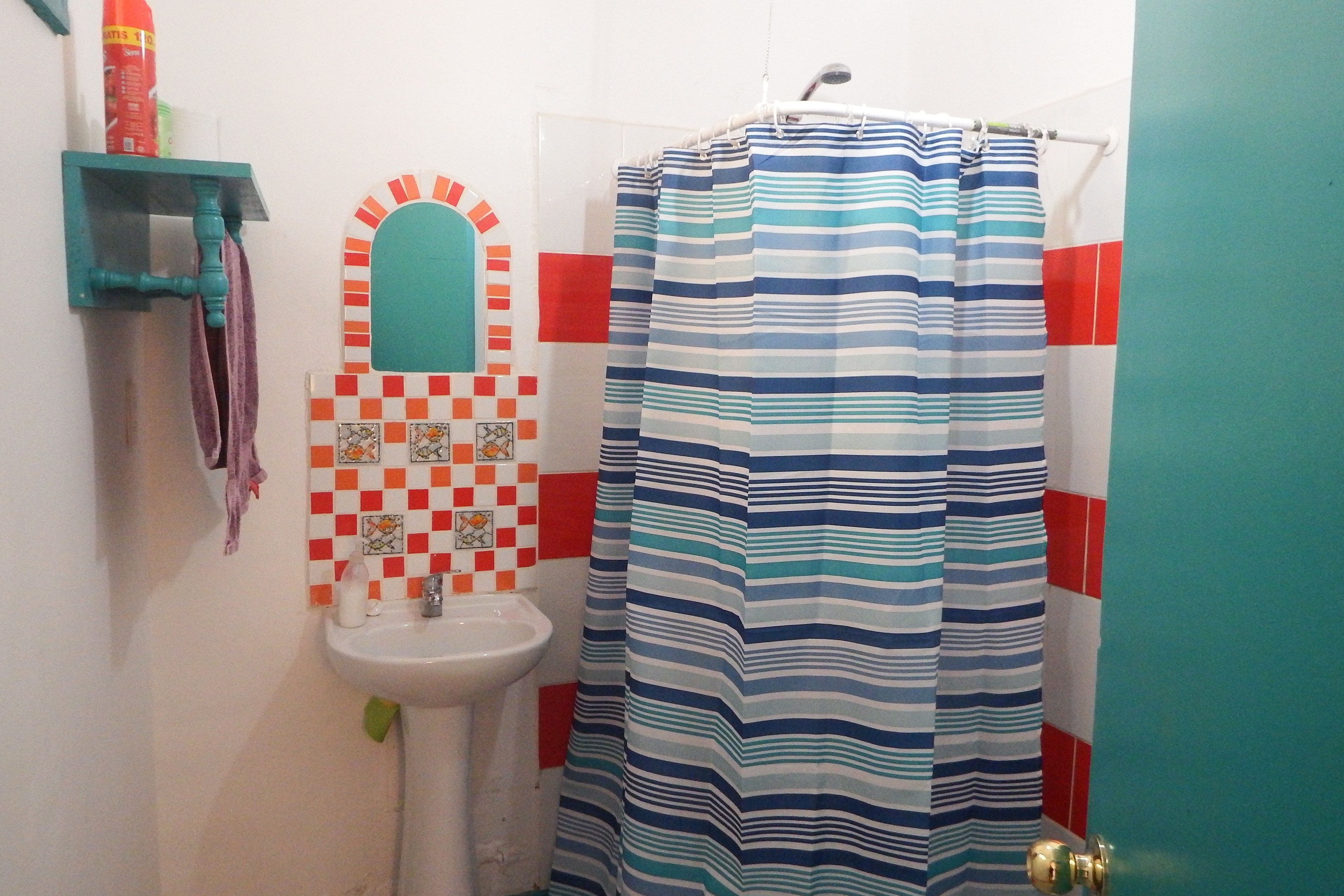 A bathroom with a striped shower curtain, a sink, a mirror with a checkered tile backsplash, and a teal door.