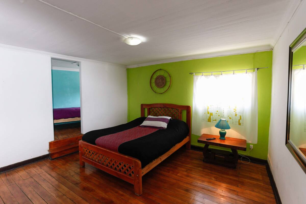 A room with a wooden bed, a nightstand with a lamp, and a window with curtains.