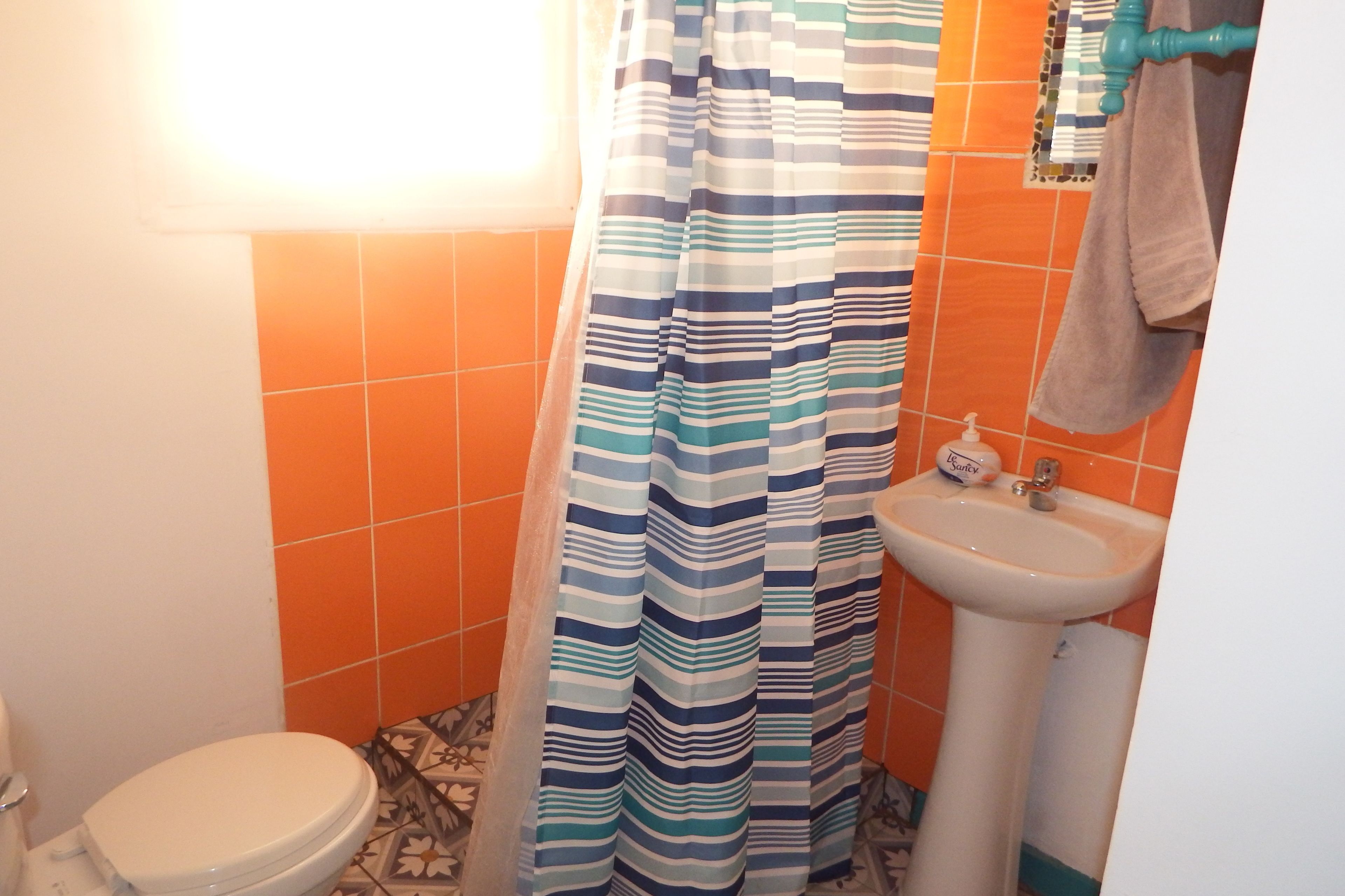 Un baño con cortina de ducha a rayas, inodoro y lavamanos con dispensador de jabón.