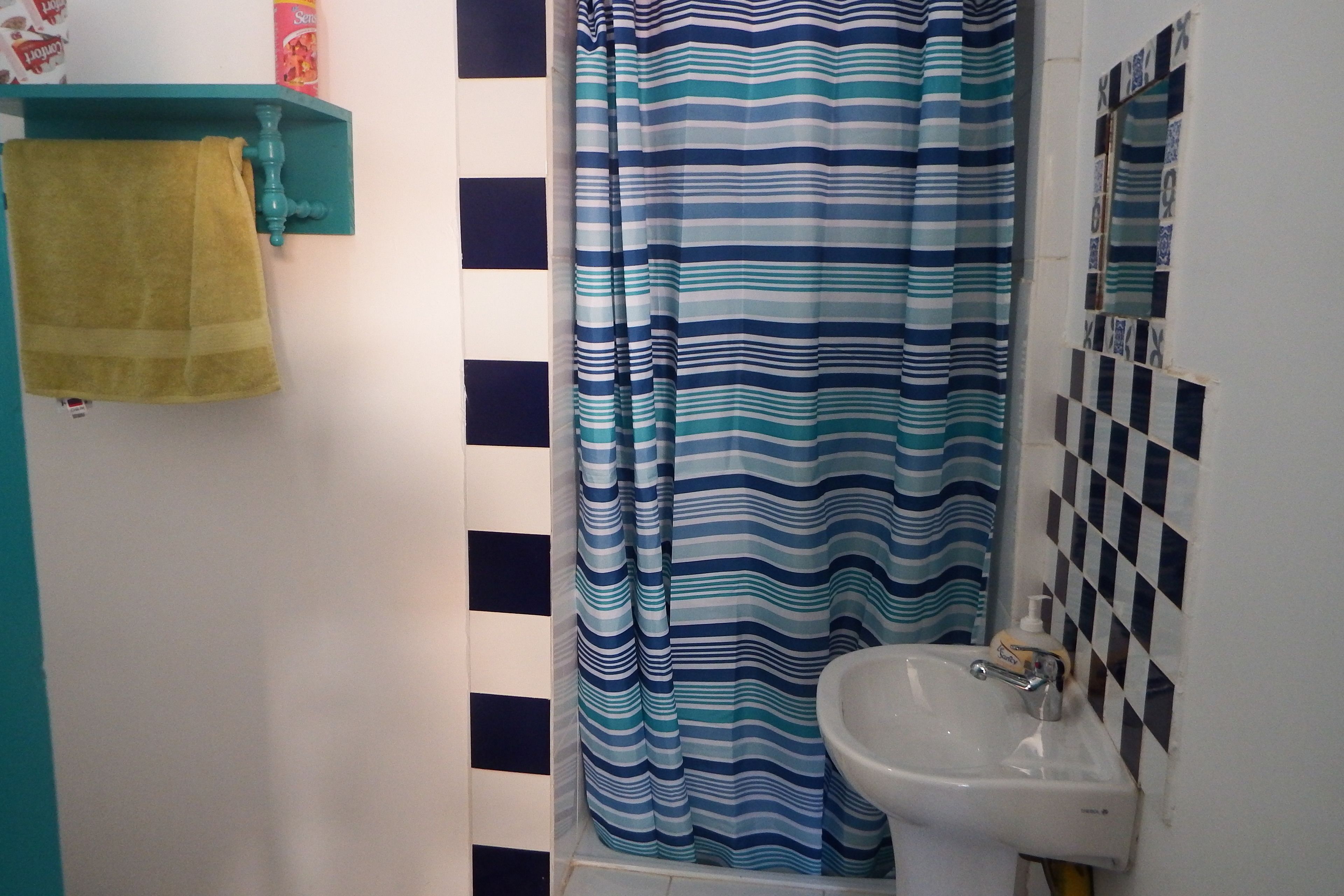 A bathroom with a striped shower curtain, a sink, and a towel hanging on a teal-colored towel rack.