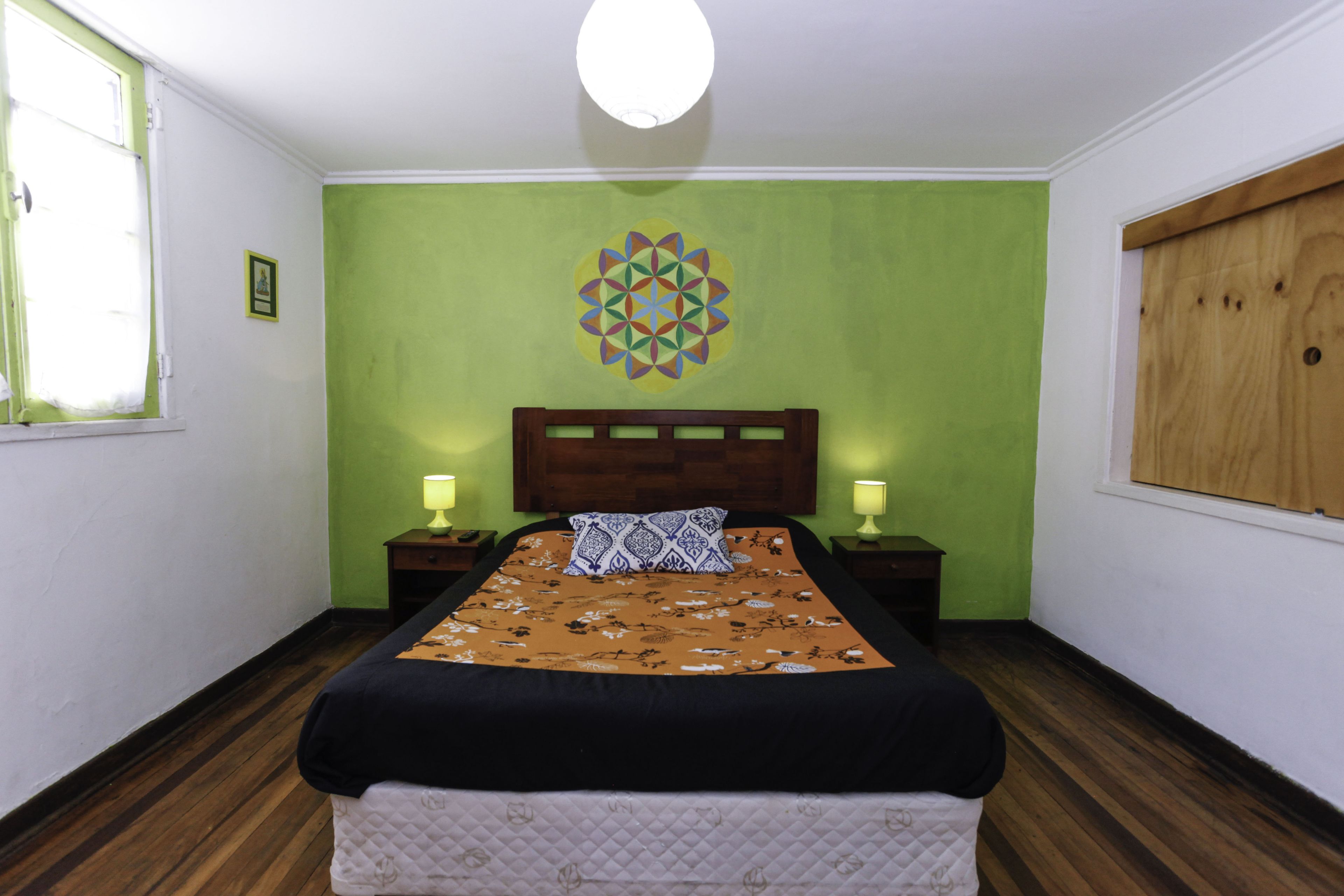 A bedroom with a bed, two bedside tables with lamps, a wooden headboard, a green wall, and a wooden floor.