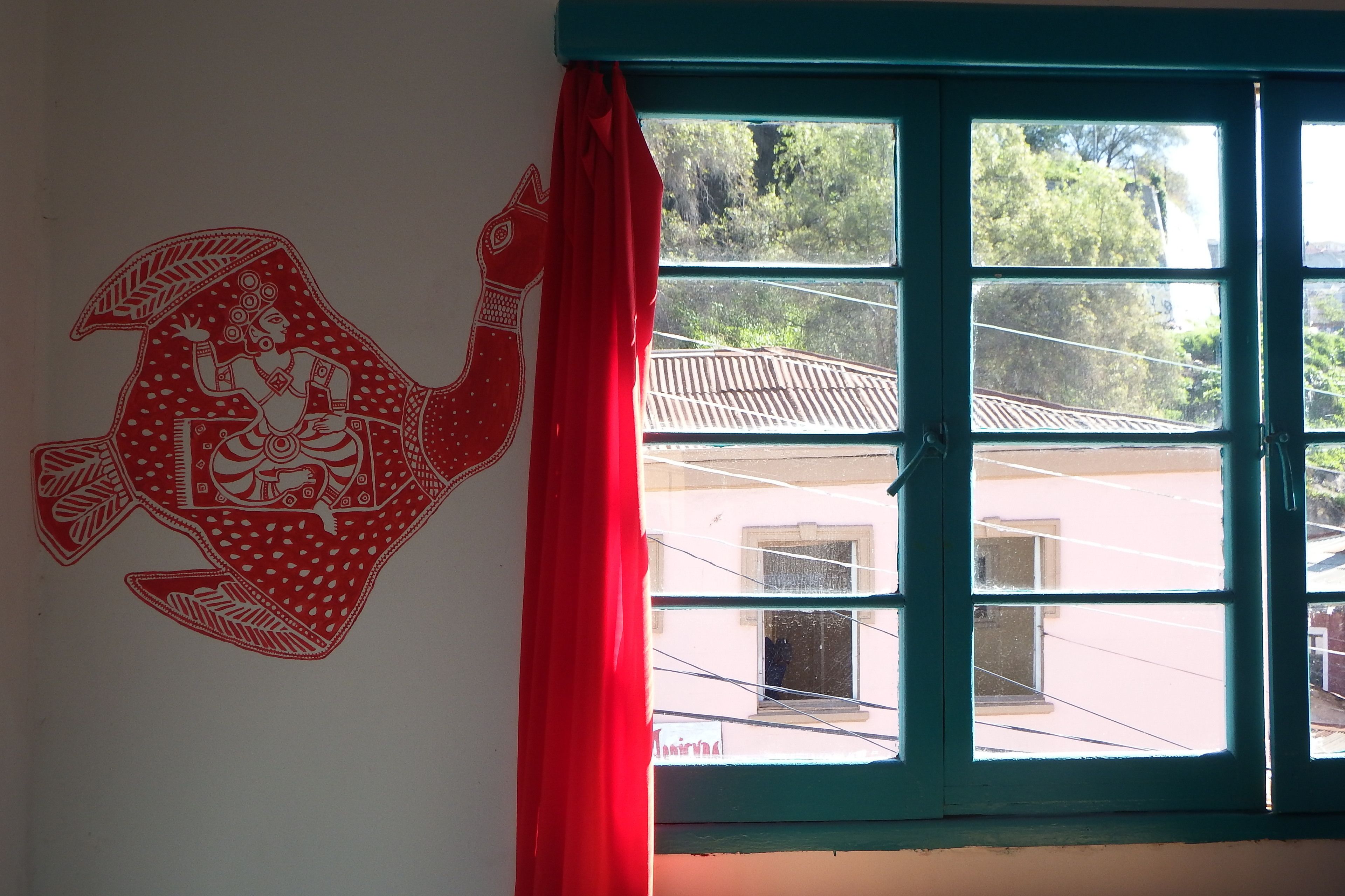 Una habitación con un ventanal grande, una cortina roja y un adorno en la pared.