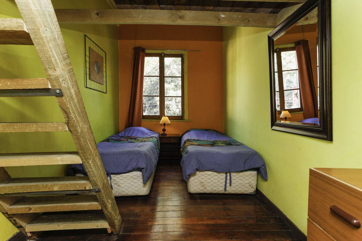 A room with two beds, a wooden ladder, a window with curtains, and a mirror on the wall.