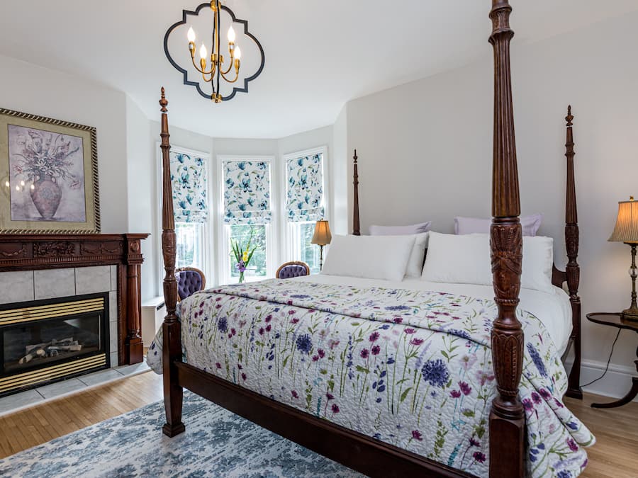 A four-poster bed with floral bedding, a fireplace, and a chandelier.