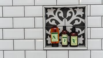 A bathroom with white tiles and a decorative black and white tile accent piece. Three bottles of body wash are displayed on a shelf.