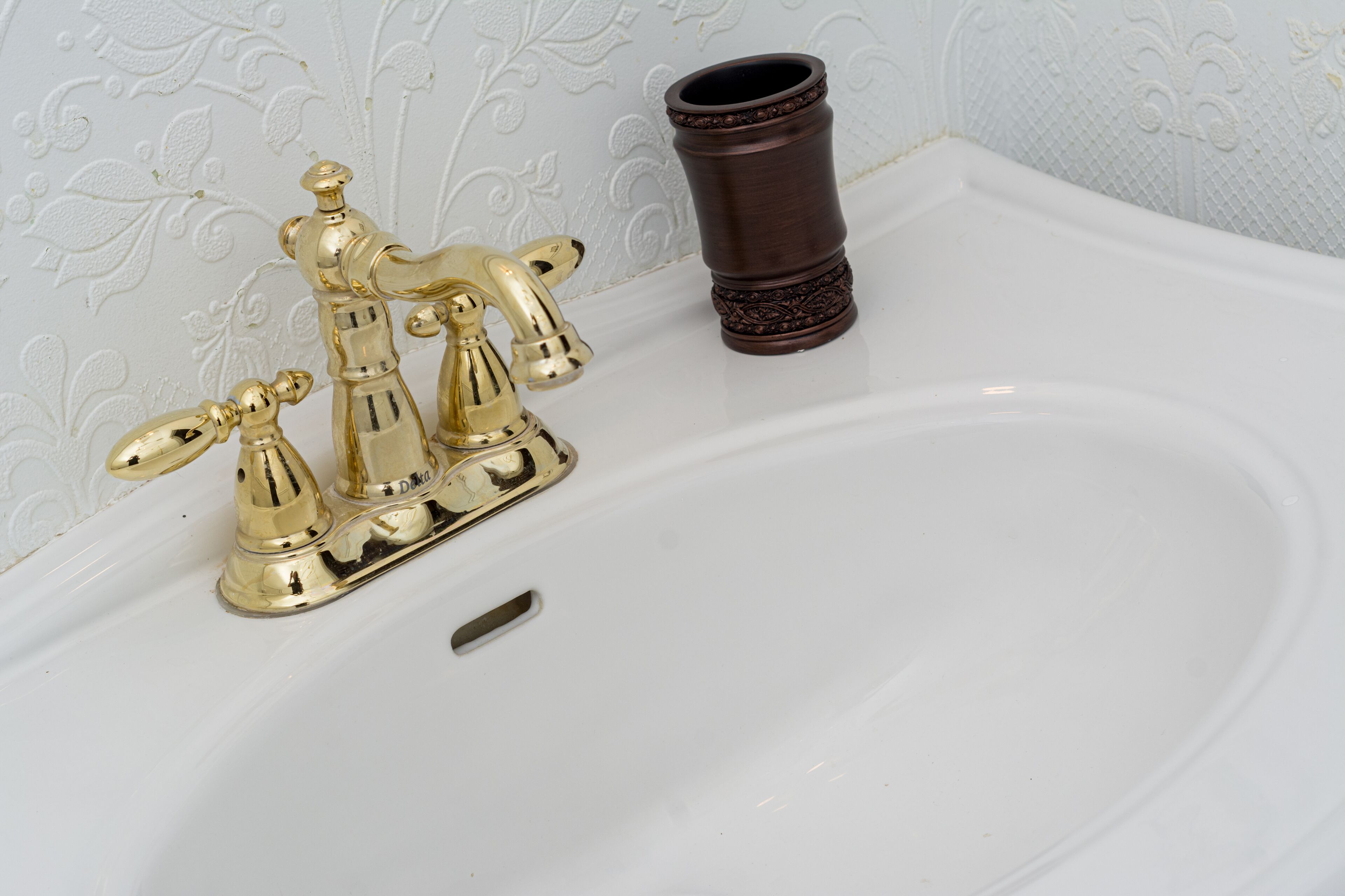 Ein weißes Waschbecken mit goldfarbenem Wasserhahn und einer braunen Vase.