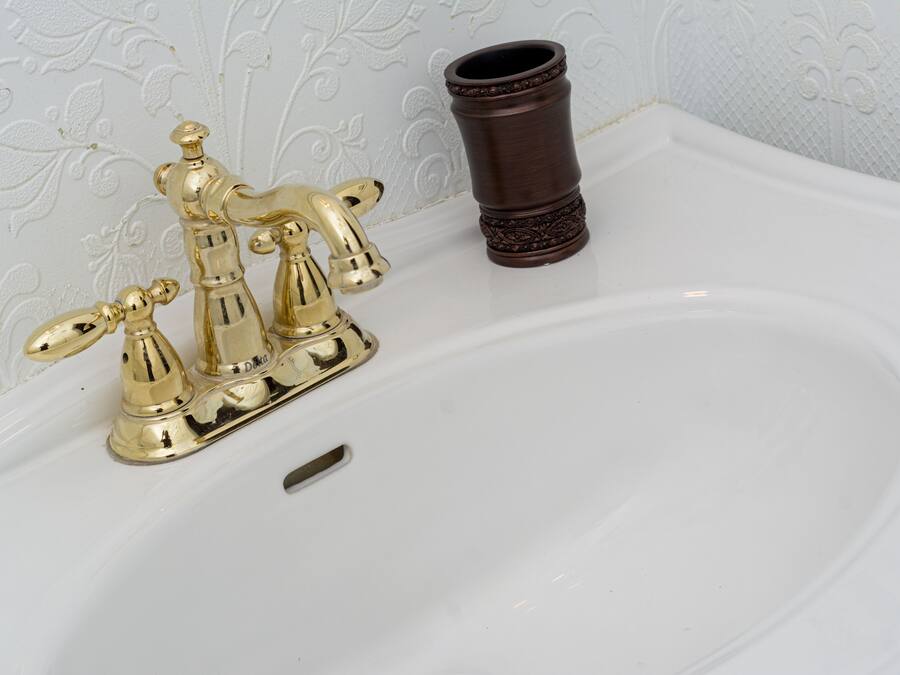 Ein weißes Waschbecken mit goldfarbenem Wasserhahn und einer braunen Vase.