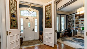 Un hall d’entrée spacieux, doté de planchers en bois, d’un lustre et d’une bibliothèque remplie de livres et d’objets décoratifs.