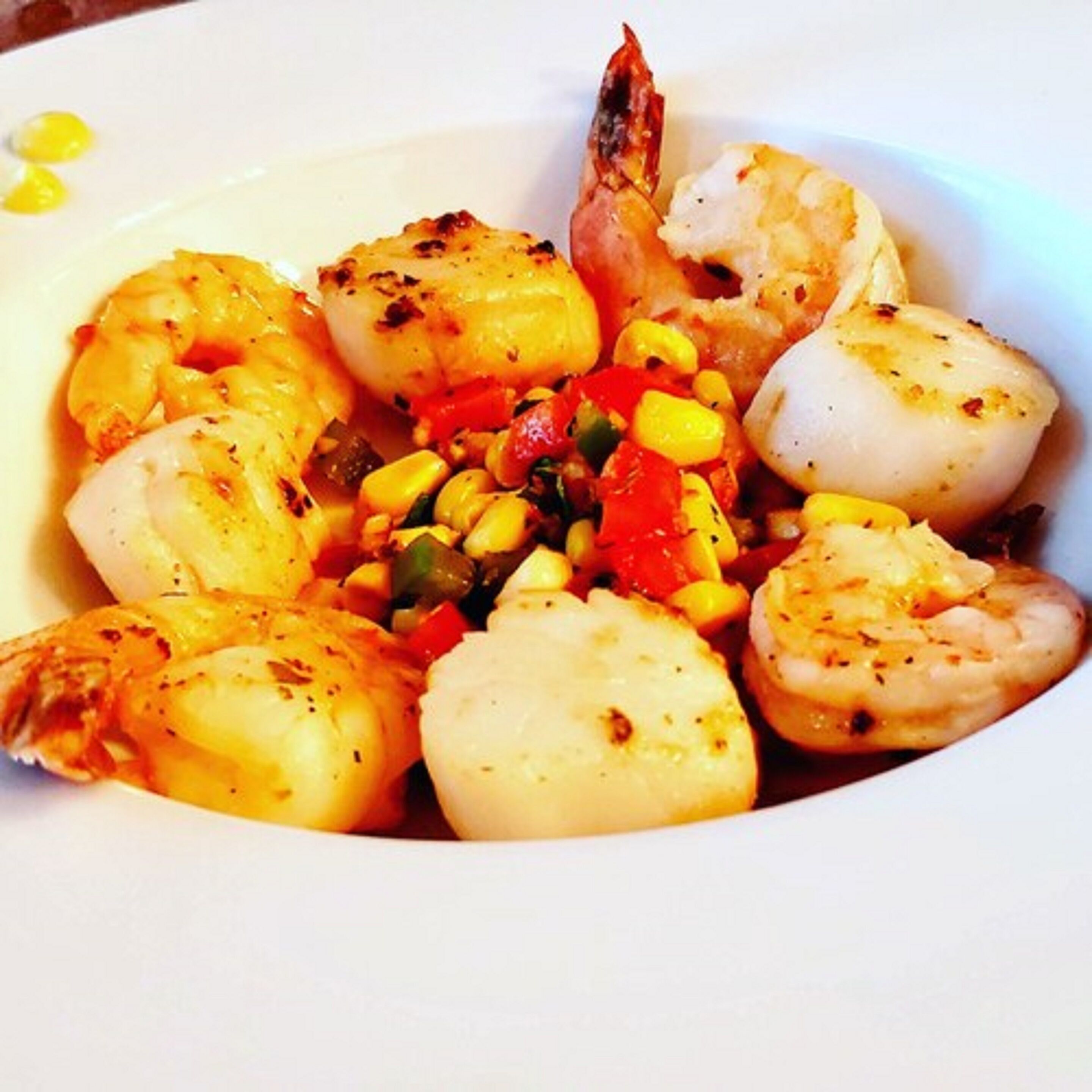 Un plato de mariscos que incluye camarones, vieiras y maíz.