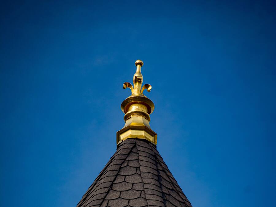 Telhado de prédio com design de telhas pontudas e escuras e um pináculo ornamental dourado.