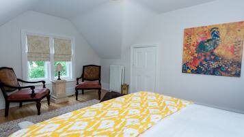 A bedroom with a bed, two chairs, a radiator, a window with blinds, and a painting on the wall.