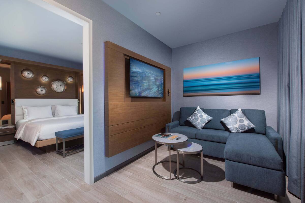 A modern hotel room with a bed, a sofa, a small table, and artwork on the walls.