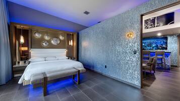 Una habitación de hotel moderna con una cama grande, una zona de estar con televisor y una pared con textura particular.