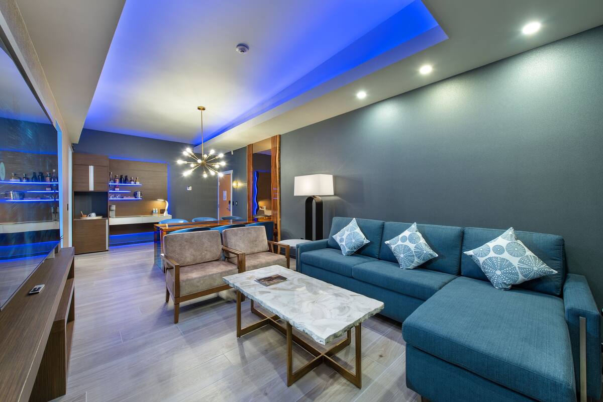 A modern living room with a blue sofa, a coffee table, and a bar area with shelves.