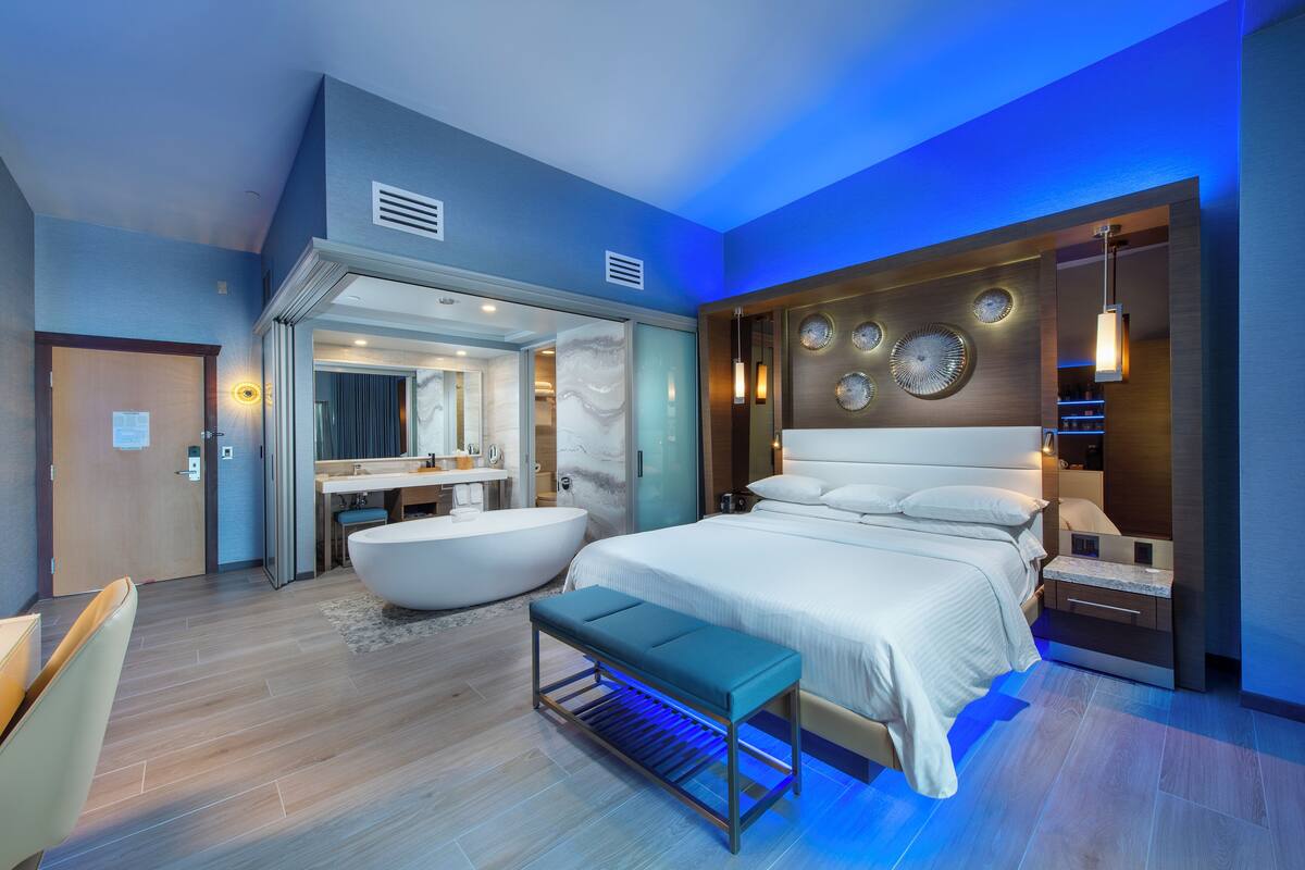 A modern bedroom with a large bed, a bathtub, and a vanity with a mirror.