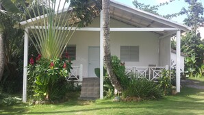 Um edifício branco com varanda coberta, cercado por vegetação exuberante e palmeiras.