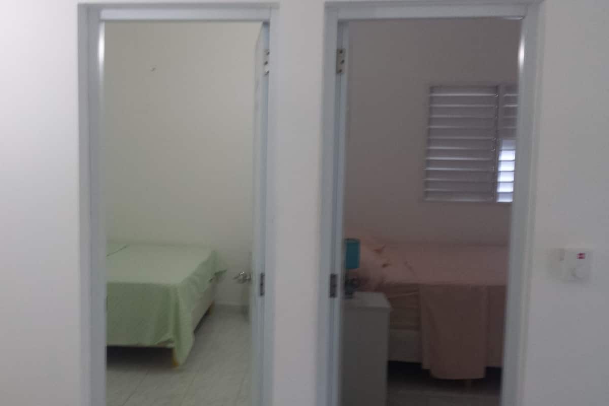 A narrow hallway leading to a bedroom with a bed and a bedside table.