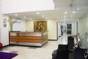 A reception area with a modern desk, a large painting on the wall, and a purple rug. - Hotel Lleras 10 (Medellín)