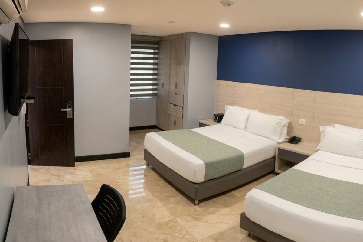A hotel room with two beds, a desk, and a chair.