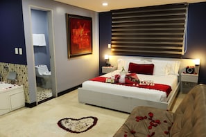 A bedroom with a bed, a nightstand, a bedside table, a bathroom, and a shower area. - Hotel Lleras 10 (Medellín)