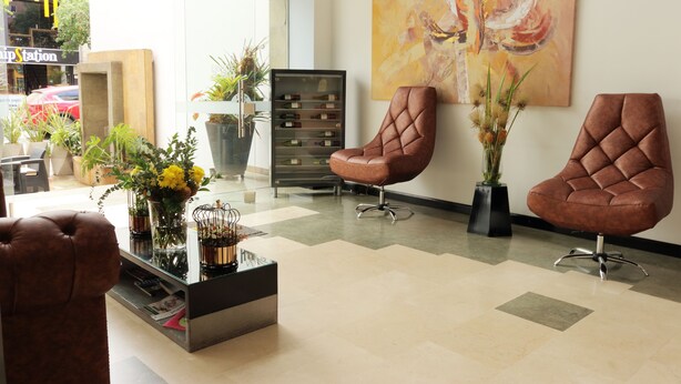 A modern lobby with leather chairs, a glass coffee table with flowers, a wine rack, and a large abstract painting on the wall. - Hotel Lleras 10 (Medellín)