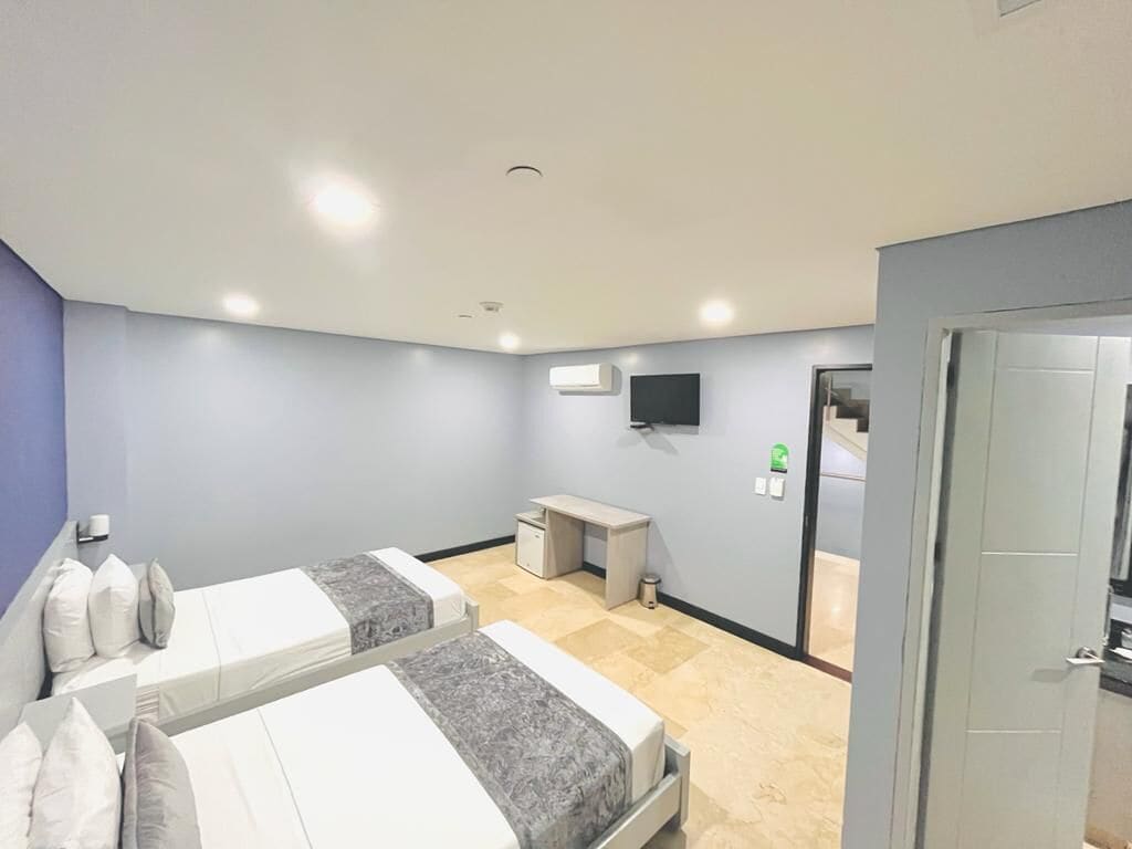 Habitación de hotel con dos camas, un escritorio, un televisor y una puerta.