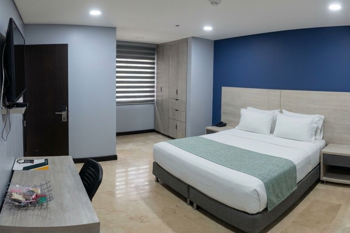 A modern hotel room with a large bed, bedside tables, a desk with a chair, and a television.
