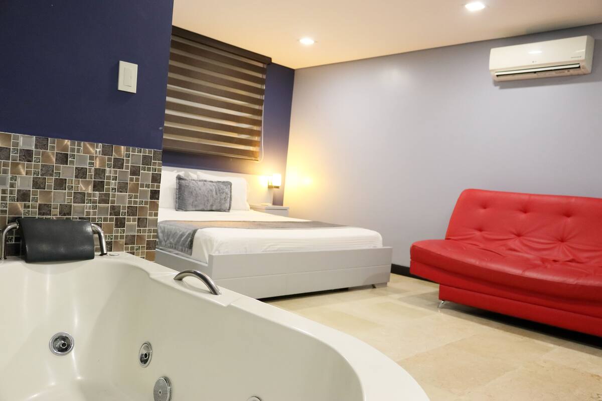 A modern bedroom with a large white bathtub, a red sofa, and a bed with a headboard.