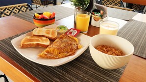 A breakfast setting with toast, an omelet, a bowl of cereal, a glass of orange juice, and a fruit bowl. - Hotel Lleras 10 (Medellín)