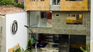 A multi-story hotel with a modern design, featuring a mix of glass and stone facade, a visible entrance, and a small outdoor seating area. - Hotel Lleras 10 (Medellín)