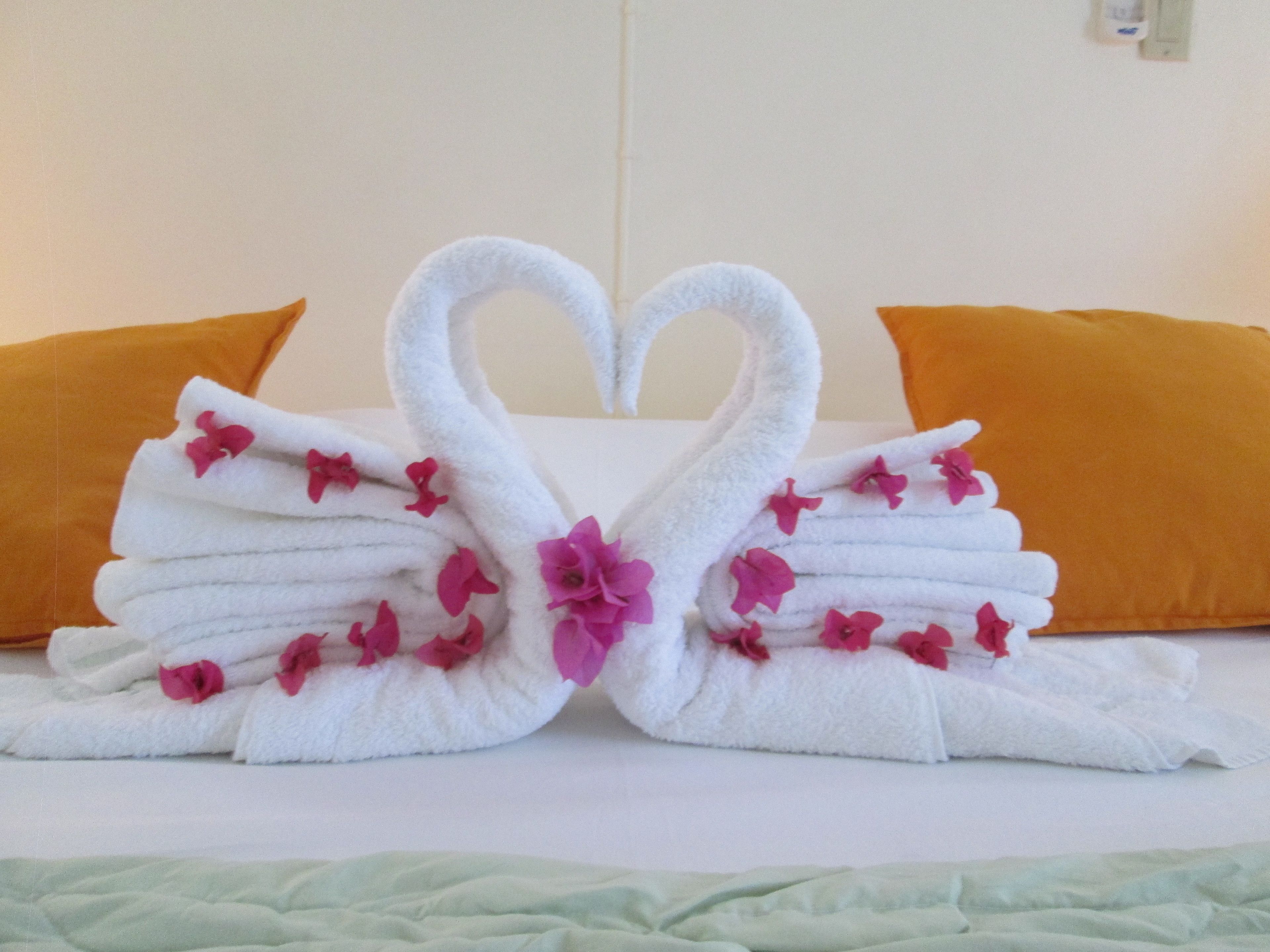 A bed with a heart-shaped towel arrangement made of white towels and pink flowers.