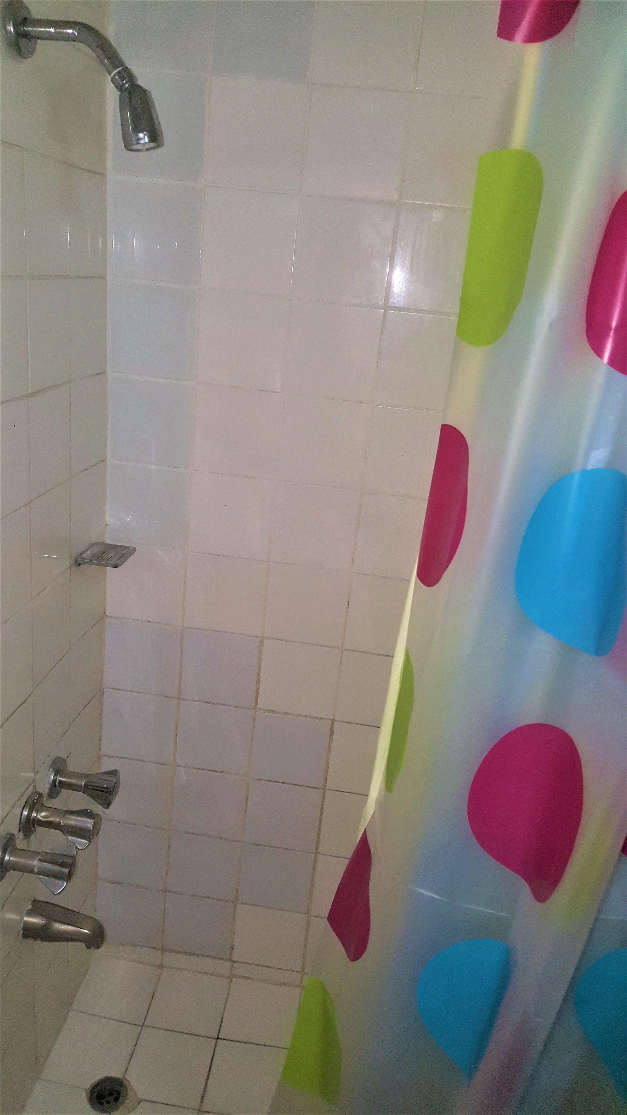 A bathroom with white tiled walls, a shower with a silver faucet, and a colorful shower curtain.