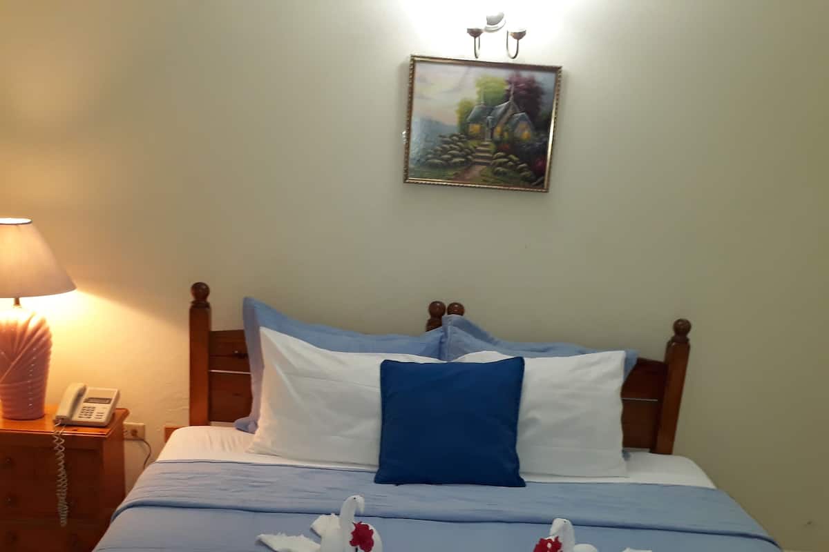 Un lit bien fait, avec une literie bleue et blanche, deux cygnes décoratifs, un tableau au mur et une lampe de chevet.