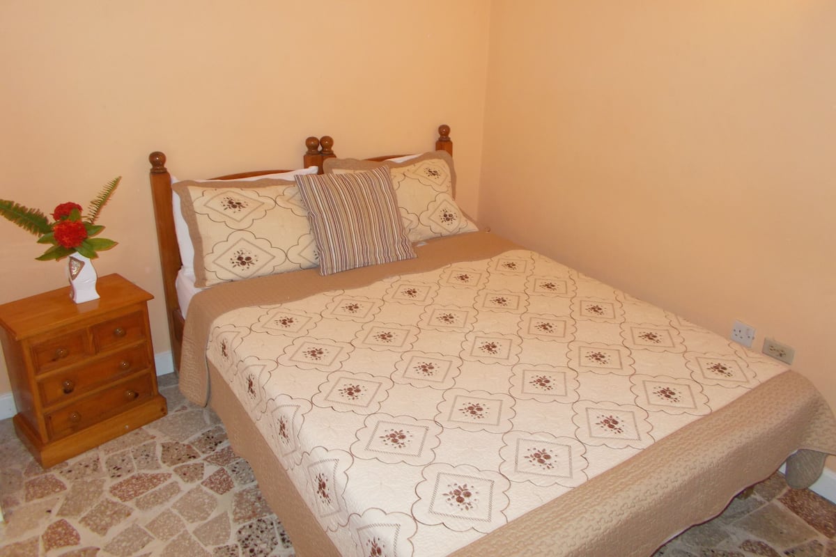 Une chambre à coucher avec un lit, une table de chevet en bois et un vase rempli de fleurs.