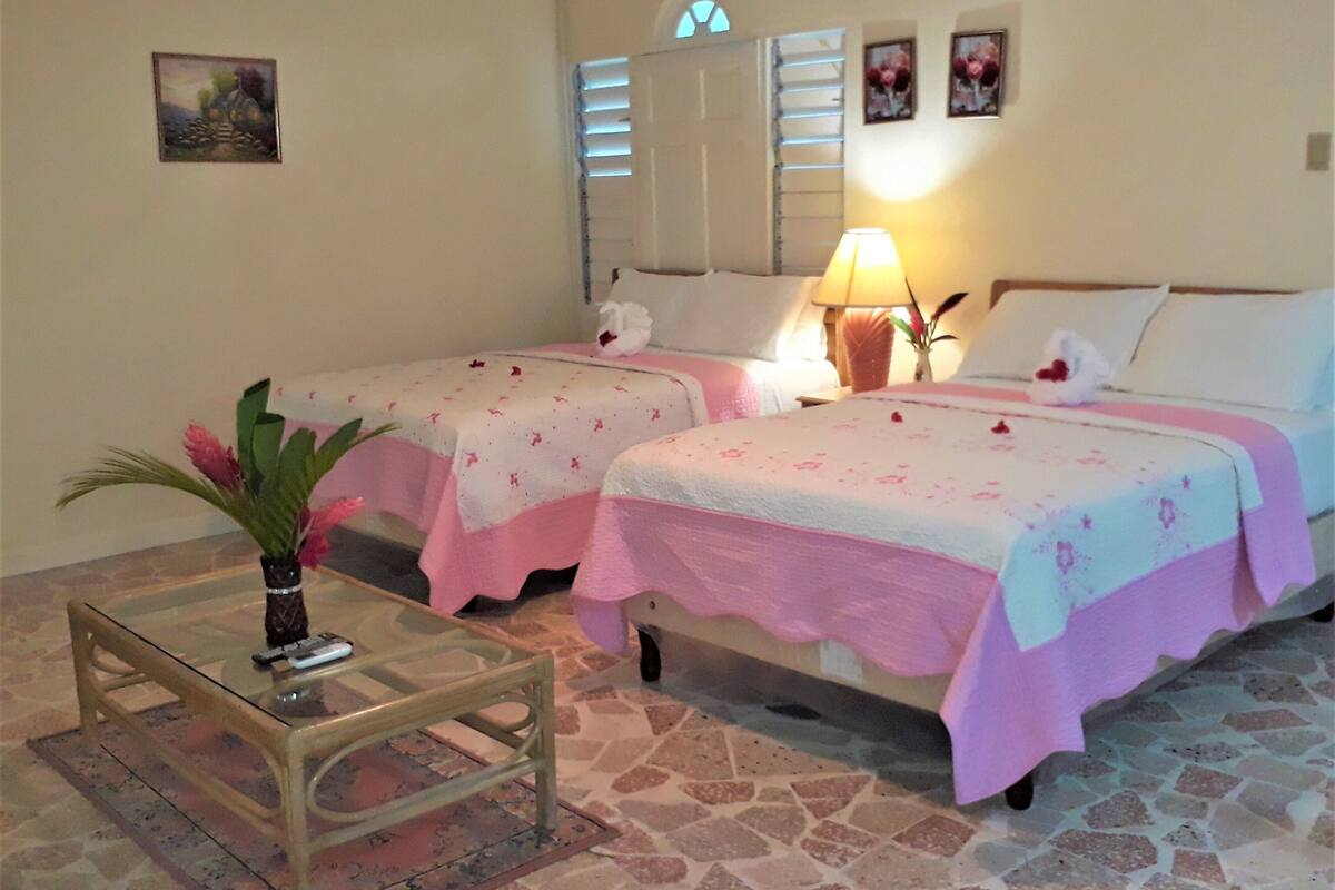 Une chambre d’hôtel avec deux lits, une petite table sur laquelle est posé un vase, et un sol carrelé en pierre.