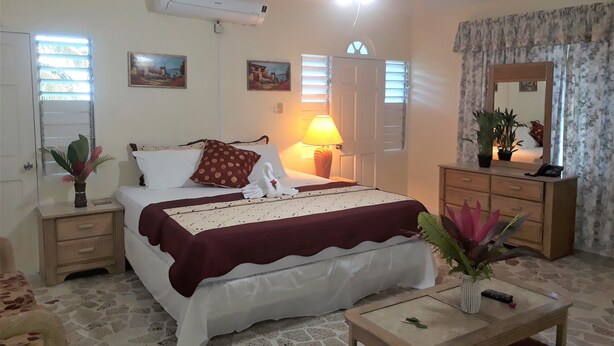 Un dormitorio con cama, mesitas de noche, cómoda, espejo, ventilador de techo y ventana con persianas.