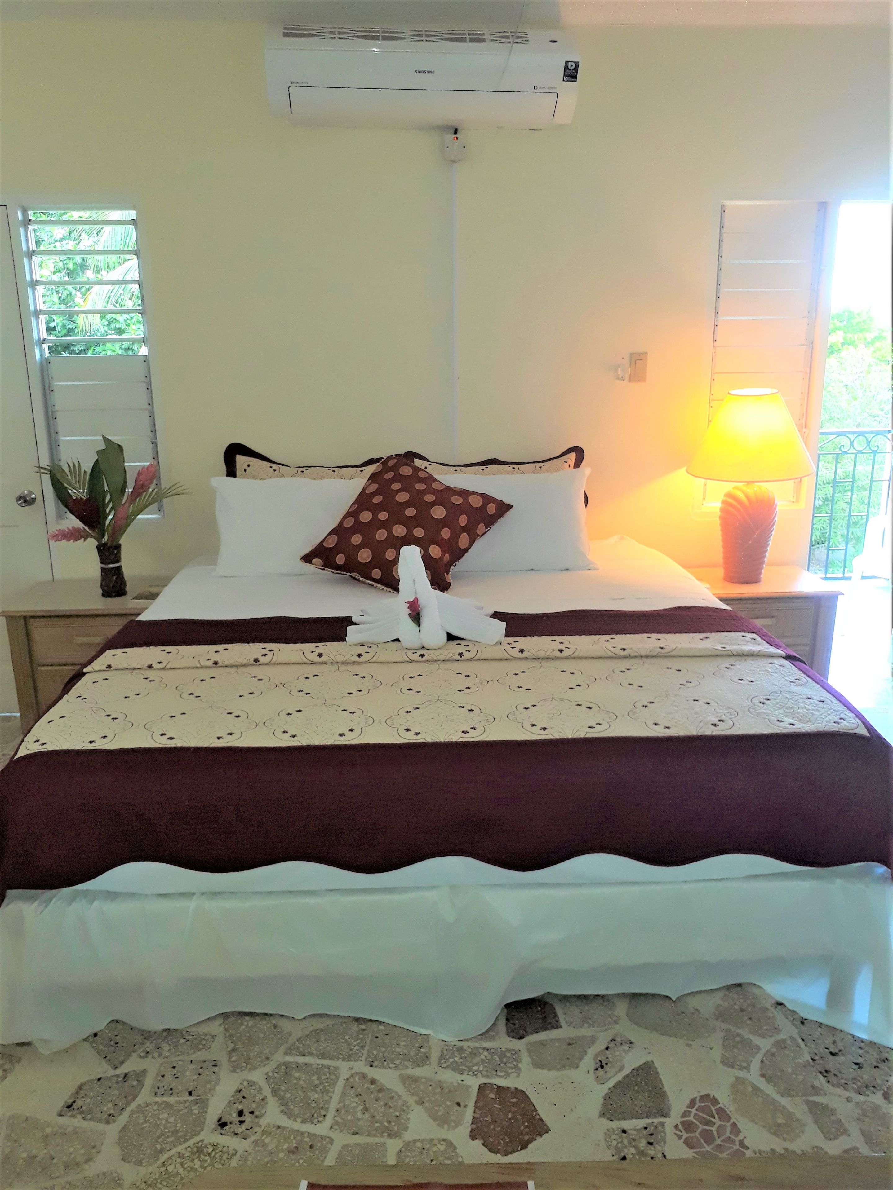 Een hotelkamer met een bed, nachtkastje, lamp, raam en airconditioning.