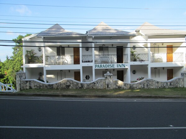Un edificio de dos pisos con un letrero que dice "Paradise Inn". Cuenta con un muro de piedra en la parte delantera, balcones en cada piso y un tejado de tejas.