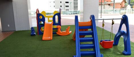 A playground with various play structures, including slides and swings, set on artificial grass.