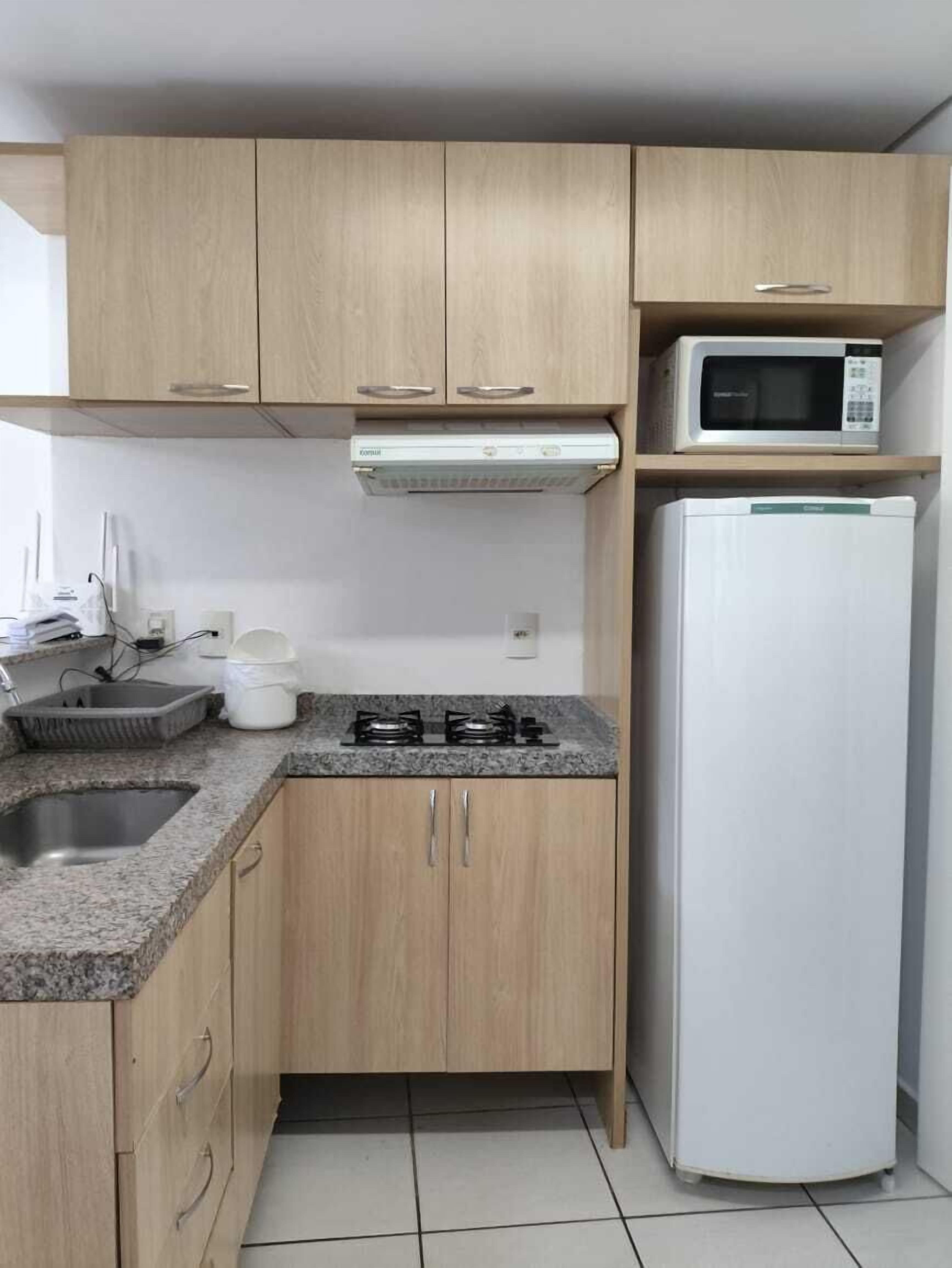 A compact kitchen with wooden cabinets, a gas stove, a microwave, and a refrigerator.
