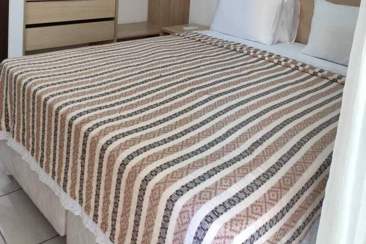 A bedroom with a bed, a wardrobe, a shelf, and an air conditioning unit.